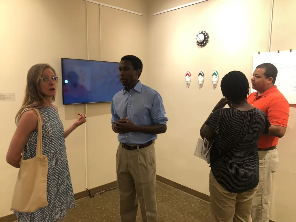 Visitors in conversation near a wall-mounted video screen in the gallery.