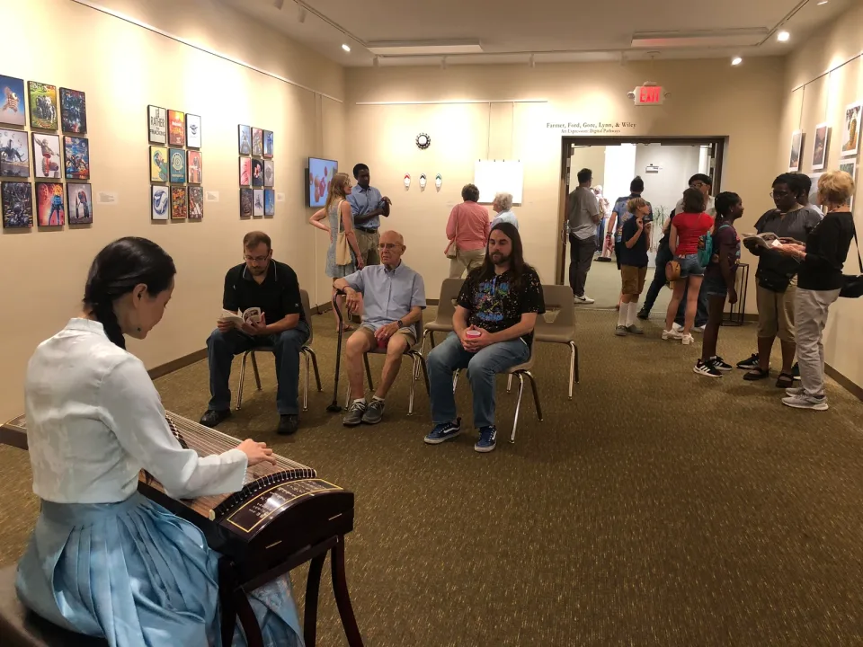 A musician performs for seated visitors, with framed artworks along the gallery walls.