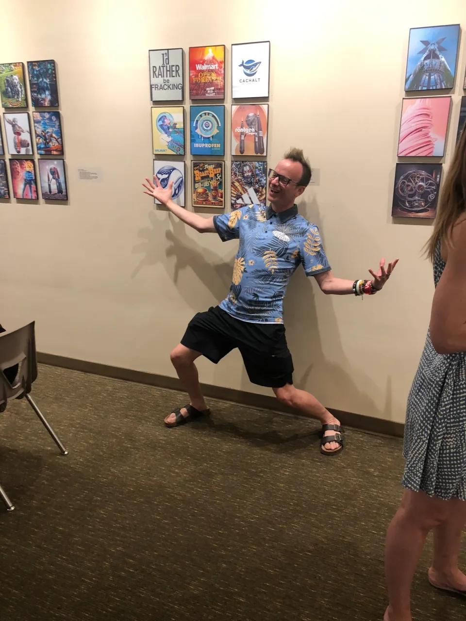 A visitor gestures toward a group of colorful framed artworks on the gallery wall.