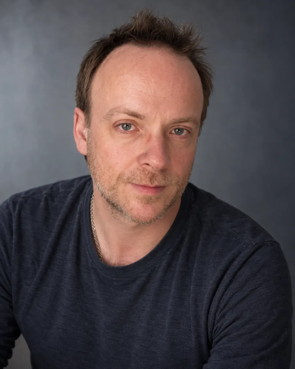 AI-assisted studio portrait of John N. Farmer, based on five supplied photographs, in a dark shirt against a quiet gray background.