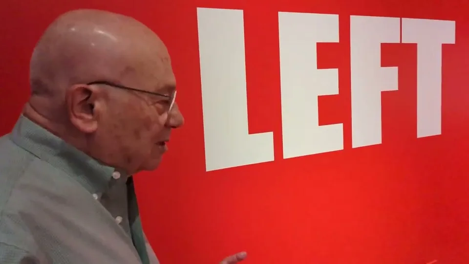 Museum-installation documentation still showing a participant beside a red wall graphic.