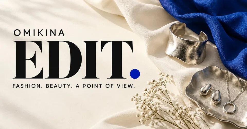 OMIKINA EDIT brand artwork with black editorial typography, a cobalt dot, ivory and blue fabric, and silver jewelry in an AI-generated still life.